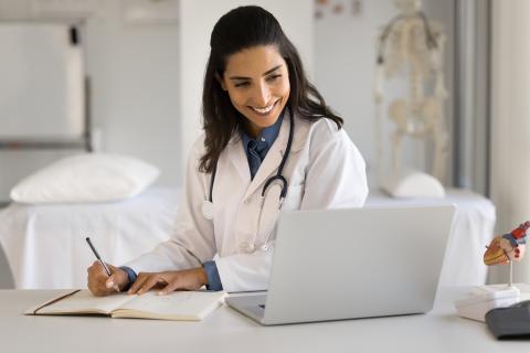 Female doctor writing note while looking at computer